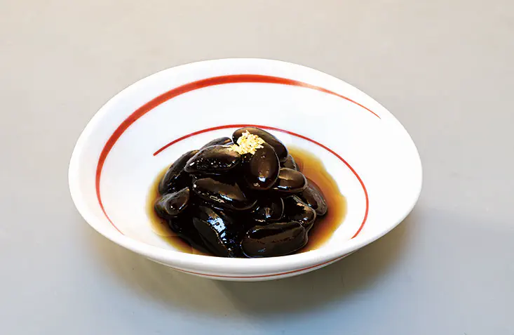なごやかセット白鳥2026のセット商品：雁食黒豆（がんくいくろまめ）を、赤色の渦巻き模様がある白い小鉢に盛り付けたイメージ。
＊丹波黒豆の代替商品として。